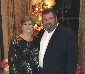 Pastor Don Bailey and his wife Sonya, smiling together in front of a Christmas tree