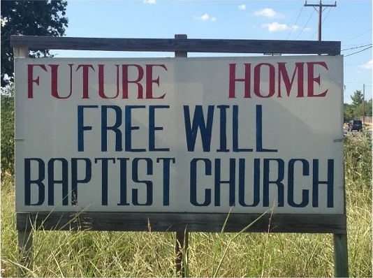 Hand-painted roadside sign reading Future Home Free Will Baptist Church, standing in tall grass under a blue Texas sky